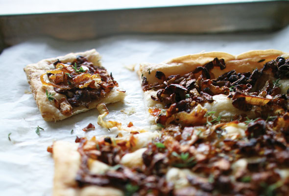 A sheet pan with n onion thyme tart on it, covered with cooked onions, thyme on a puff pastry crust