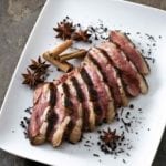 Sliced tea-smoked duck breast on a square white plate with star anise and loose tea
