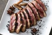 Sliced tea-smoked duck breast on a square white plate with star anise and loose tea