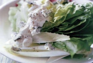 Bibb wedges with blue cheese dressing and blue cheese crumbles on a white plate.
