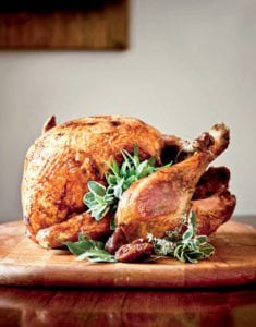 A whole deep-fried turkey, garnished with sage, bay, and thyme leaves on a wooden cutting board.