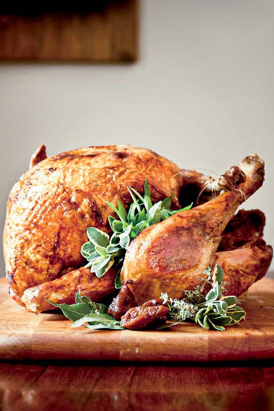 A whole deep-fried turkey, garnished with sage, bay, and thyme leaves on a wooden cutting board.