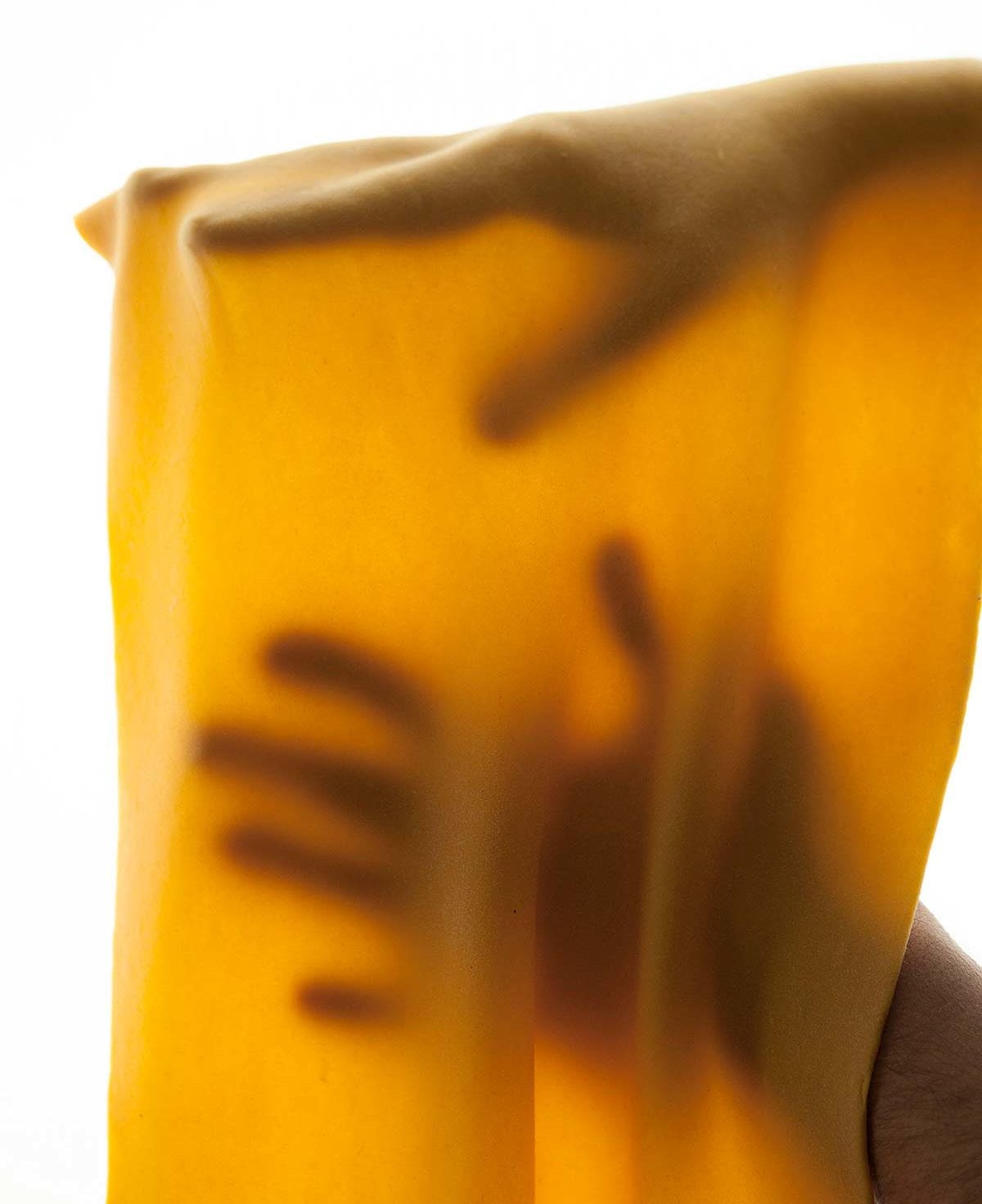 A thin sheet of pumpkin pasta dough draped over a person's hands.
