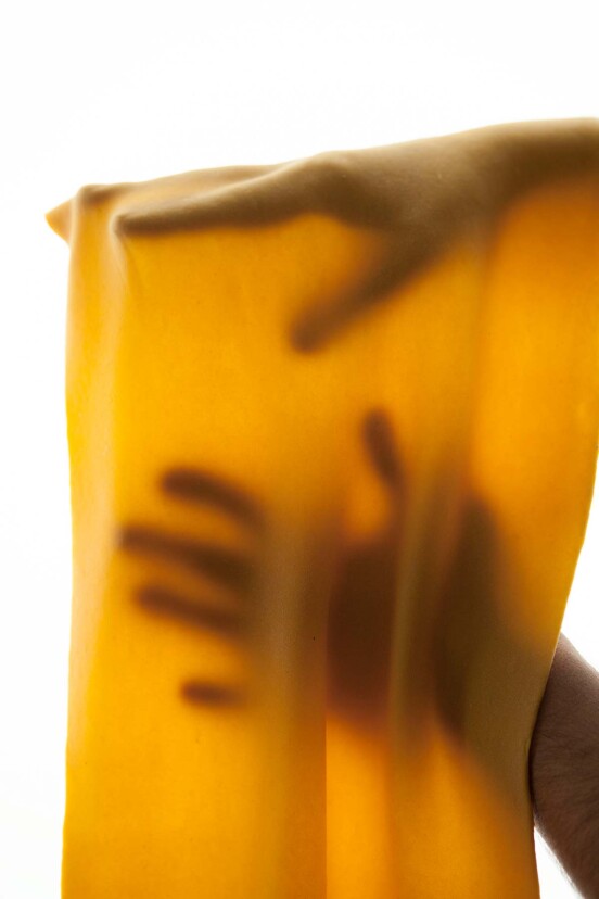 A thin sheet of pumpkin pasta dough draped over a person's hands.