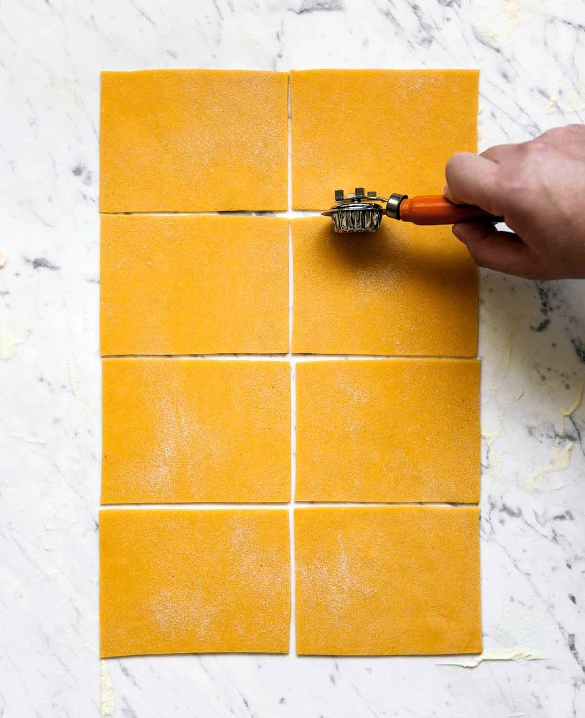 A person cutting a sheet of pumpkin pasta dough into rectangles.