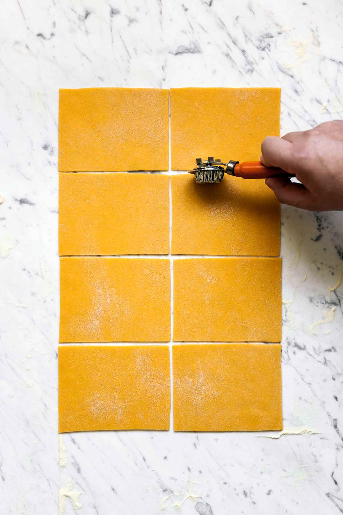 A person cutting a sheet of pumpkin pasta dough into rectangles.