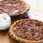 Two Southern pecan pies in pie plates with a bowl of whipped cream in between them.