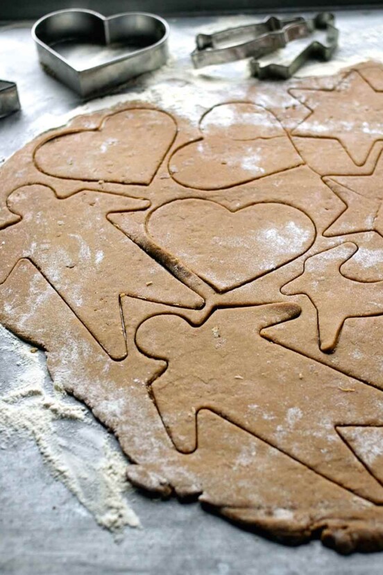 A sheet of raw black pepper cookie dough with shapes--men, stars reindeer, hearts--cut into it
