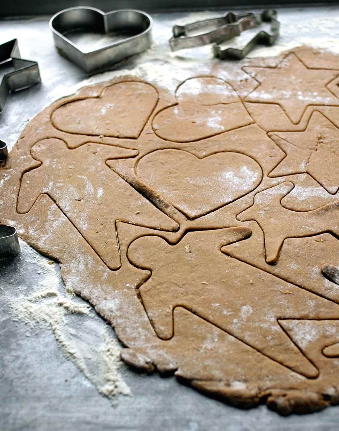 A sheet of raw black pepper cookie dough with shapes--men, stars reindeer, hearts--cut into it