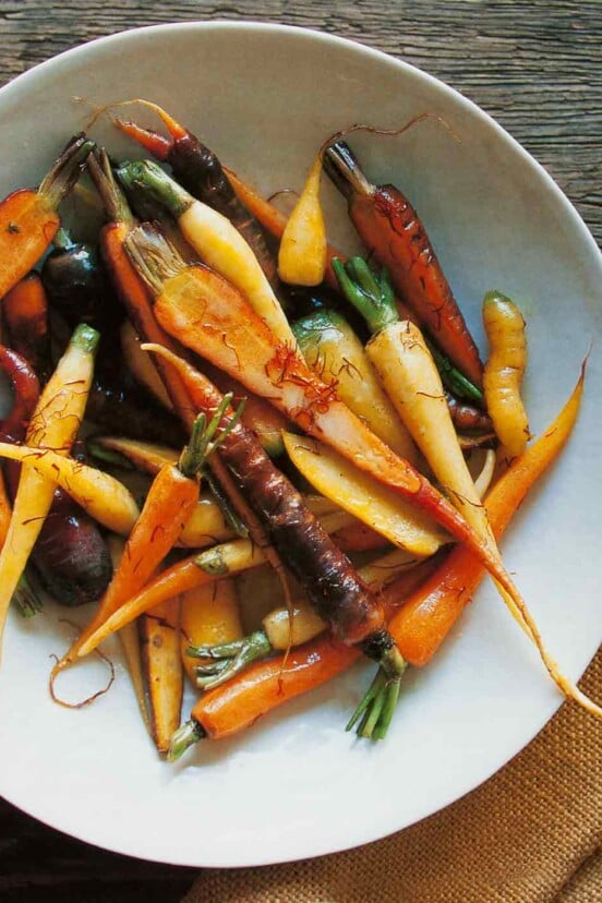 A white bowl of braised saffron carrots on a piece of burlap on a wooden table.
