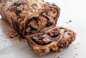 A loaf of chocolate babka on a sheet of parchment with one slice cut off.