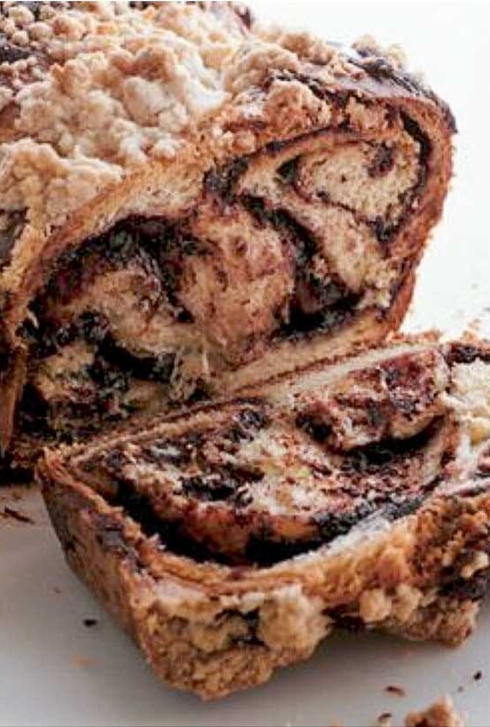A loaf of chocolate babka on a sheet of parchment with one slice cut off.