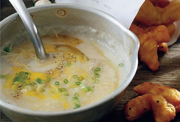 A bowl of congee garnished with scallions and freshly ground black pepper with some fritters on the side.