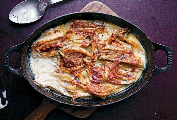 A cast-iron baking dish filled with fennel baked in cream on a wooden board.