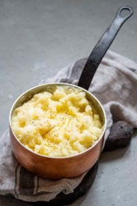 Garlic mashed potatoes with melted butter and black pepper inside a copper pot, resting on a kitchen towel.