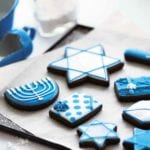 A selection of frosted cookies decorated for Hanukkah, on a parchment-lined cookie sheet