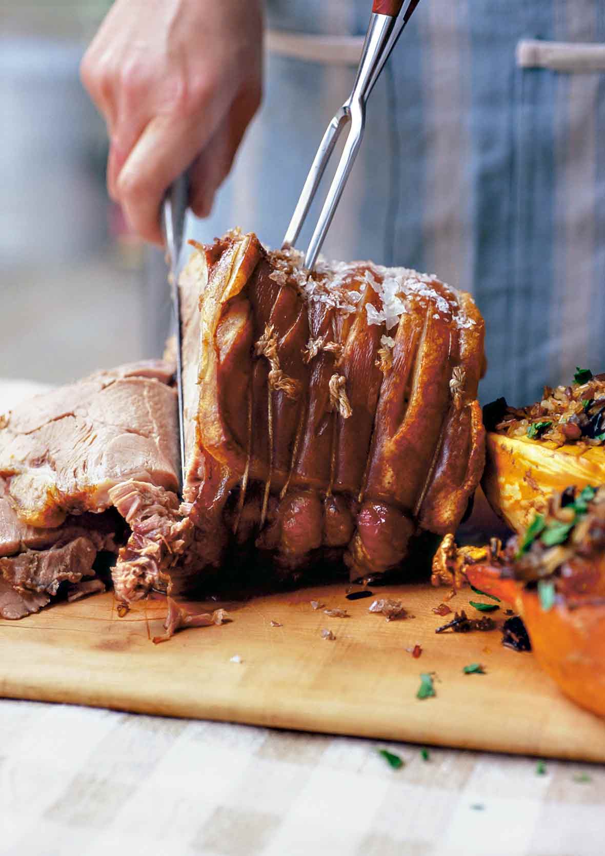 Slow-roasted pork shoulder on a cutting board being sliced by a person, flanked by two stuffed squash halves.