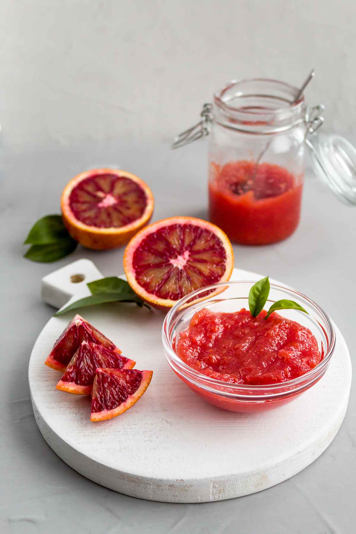 A bowl of blood orange marmalade with slices of oranges on a round marble tray.