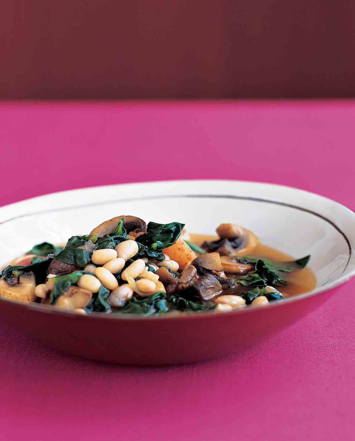 A bowl chicken, navy bean, and spinach stew on a pink tabletop.