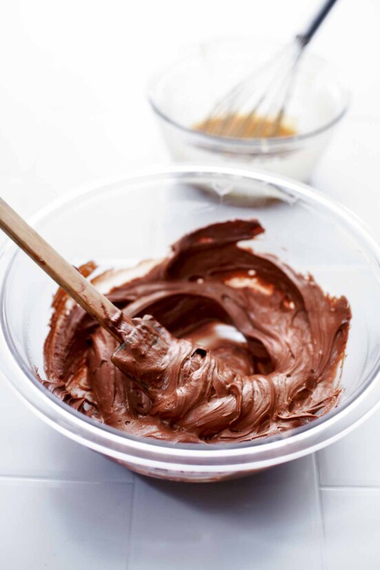 A glass mixing bowl filled with homemade nutella and a spatula rests inside the bowl