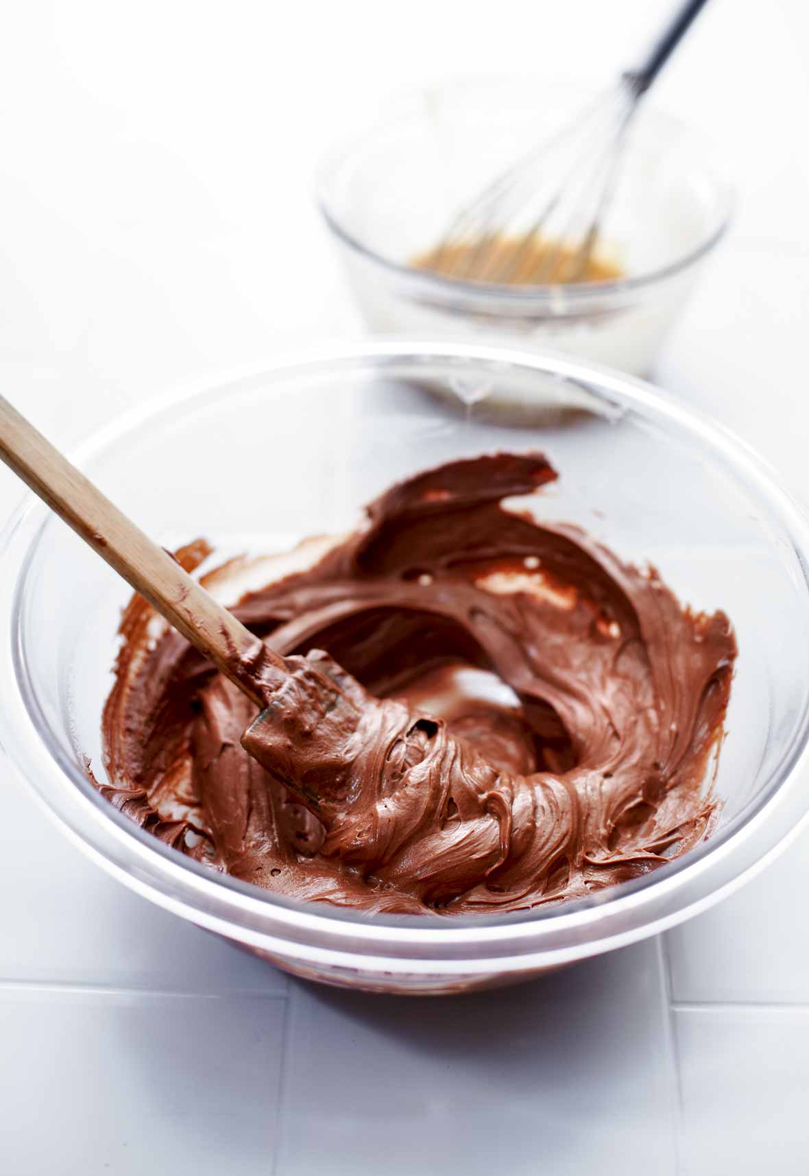 A glass mixing bowl filled with homemade nutella and a spatula rests inside the bowl