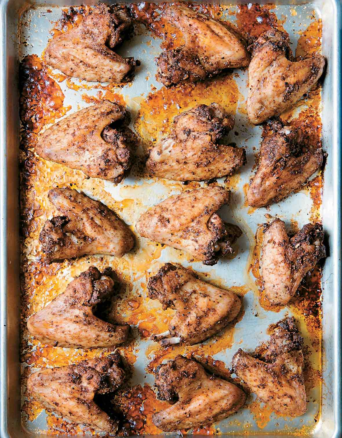 A rimmed baking sheet filled with peppery chicken wings