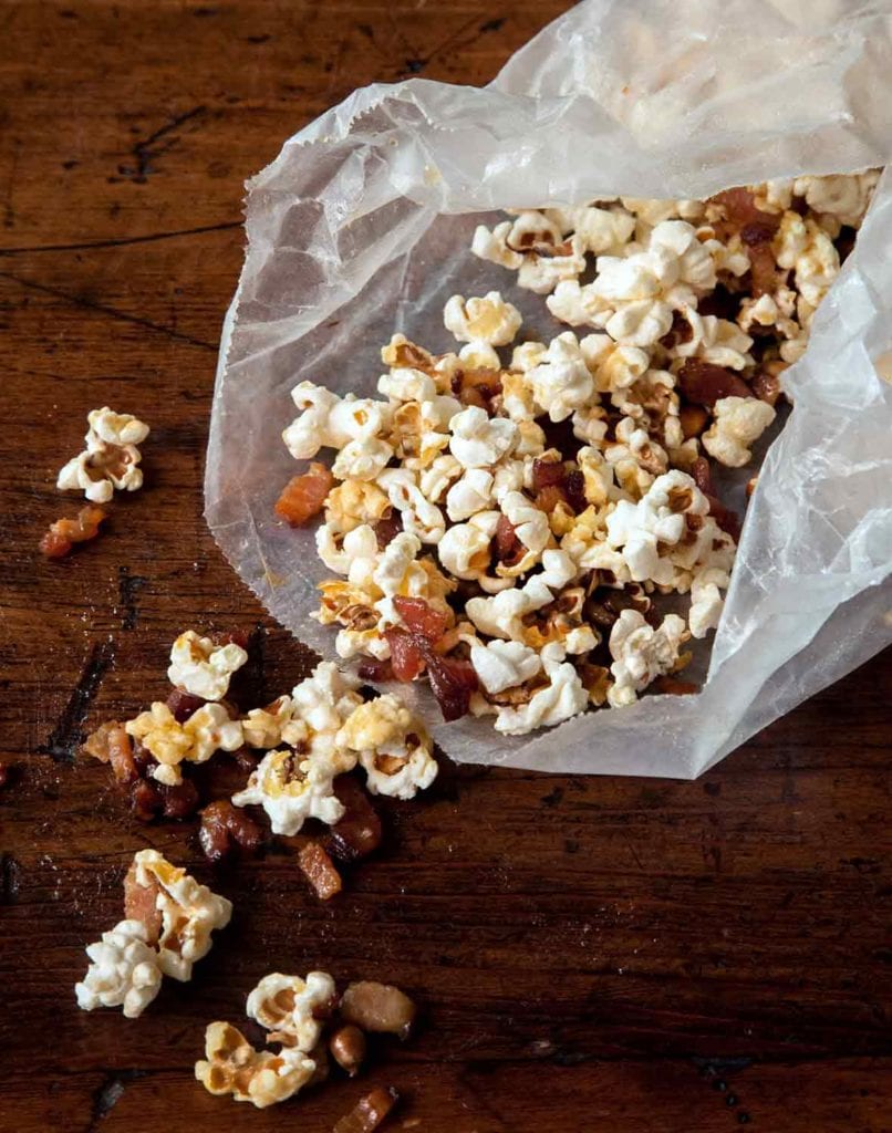 Open waxed paper bag with popcorn and maple bacon bits spilling out