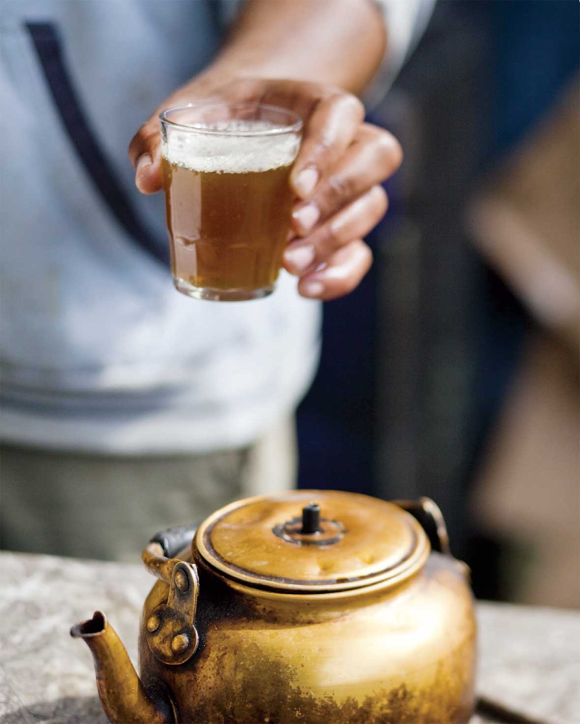 A tumbler filled with amber liquid and a teapot in the foreground.