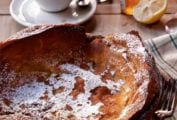 Cast-iron skillet with a Dutch baby--a popover pancake--topped with powder sugar on a set breakfast table