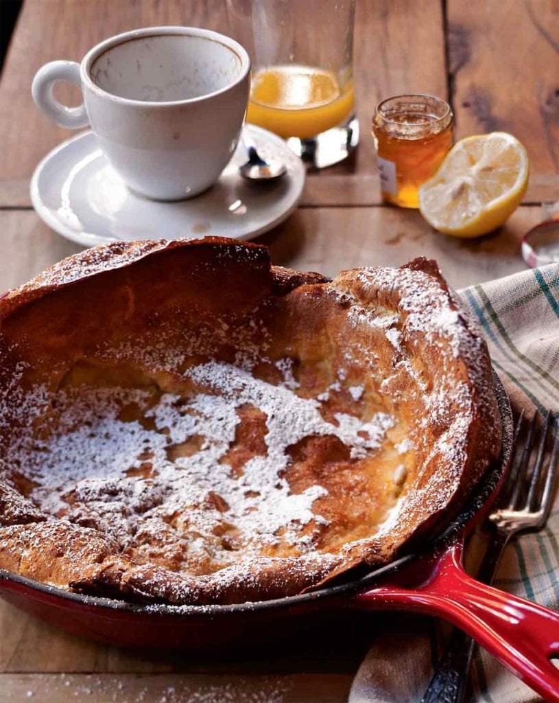 Cast-iron skillet with a Dutch baby--a popover pancake--topped with powder sugar on a set breakfast table
