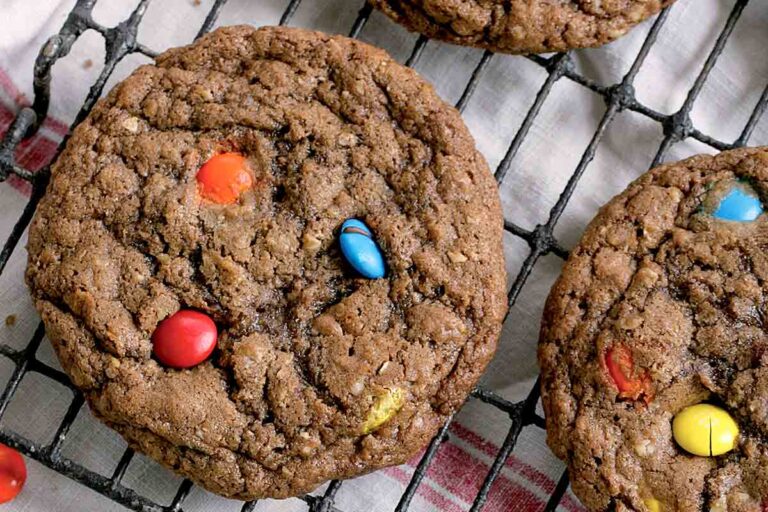Three monster chocolate M&M cookies on a cooling rack