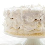 A 3-layer coconut angel food cake covered in white frosting on a white cake stand