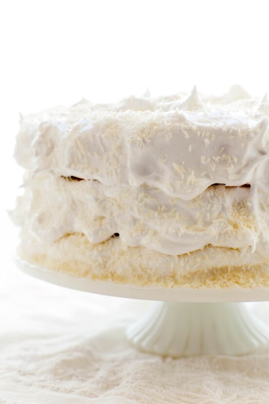 A 3-layer coconut angel food cake covered in white frosting on a white cake stand