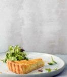 A slice of a creamy onion tart, with a flaky crust and tossed mixed salad on a white plate.