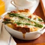 A white oval casserole filled with asparagus, egg and cheese strata--bread, Fontina cheese, eggs, prosciutto, and asparagus