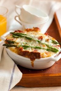 A white oval casserole filled with asparagus, egg and cheese strata--bread, Fontina cheese, eggs, prosciutto, and asparagus