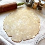 An uncooked pie crust rolled out on a floured surface with a rolling pin alongside