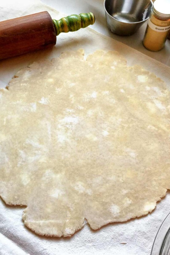 An uncooked pie crust rolled out on a floured surface with a rolling pin alongside.