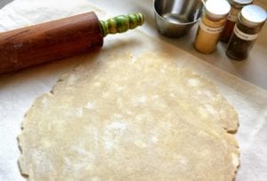 An uncooked pie crust rolled out on a floured surface with a rolling pin alongside