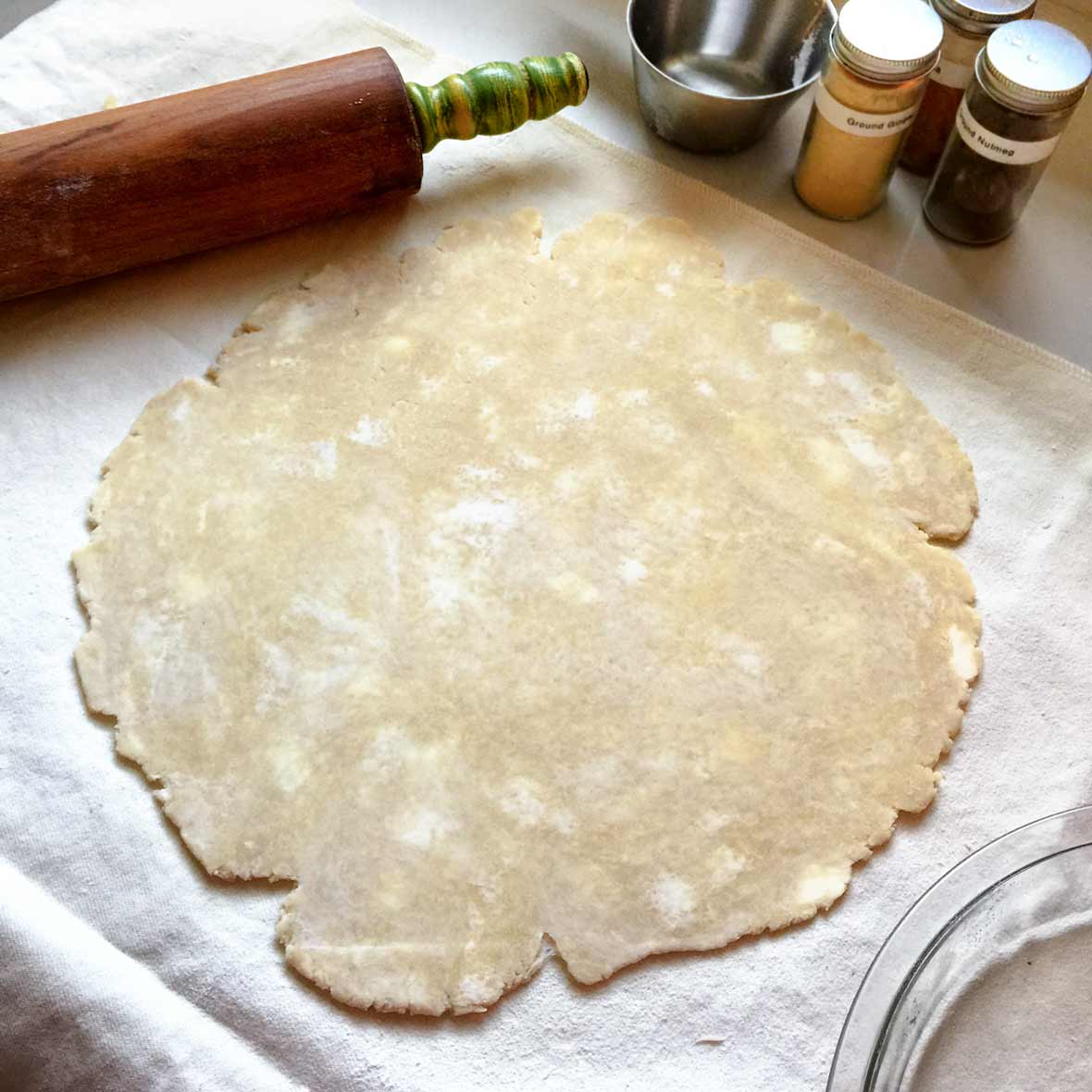An uncooked pie crust rolled out on a floured surface with a rolling pin alongside.