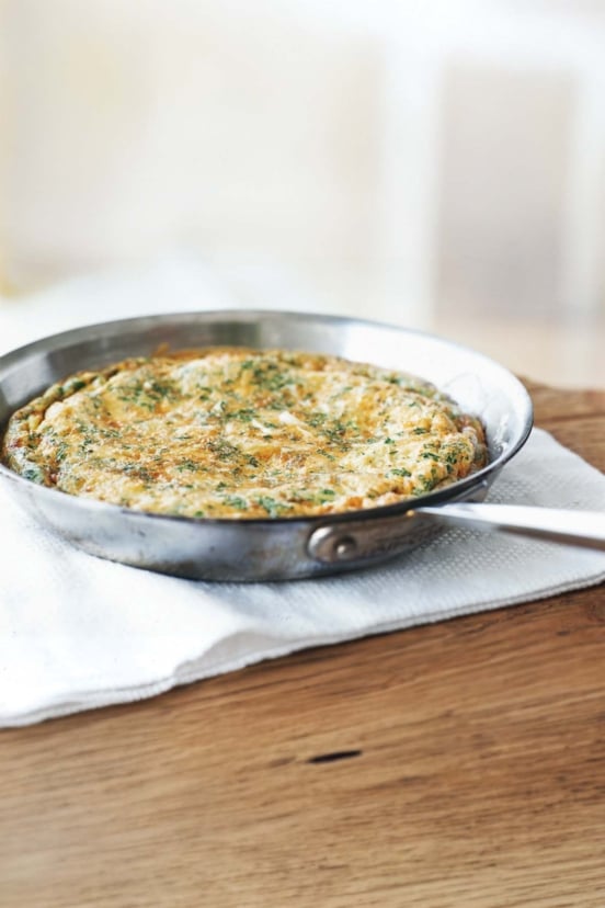 A frittata with leeks and herbs in a skillet cooling on a table.
