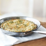 A skillet of a frittata with leeks and sprinkled with herbs on a while kitchen towel.