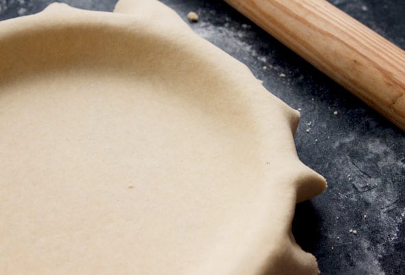 Pâte brisée draped in a pie plate with a wooden rolling pin next to it.