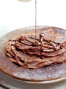 A stack of Tom Aikens' chocolate crepes being drizzled with chocolate sauce.