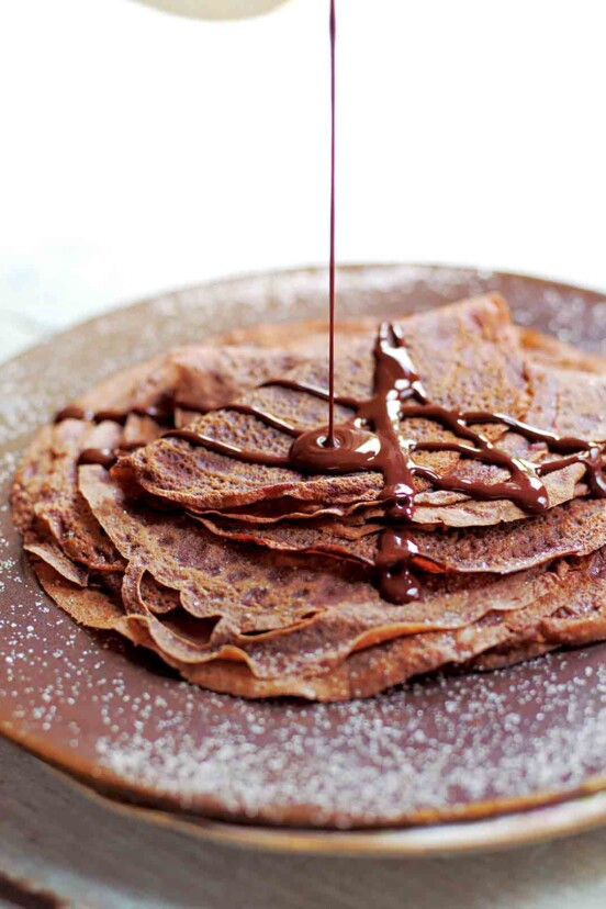 A stack of Tom Aikens' chocolate crepes being drizzled with chocolate sauce.