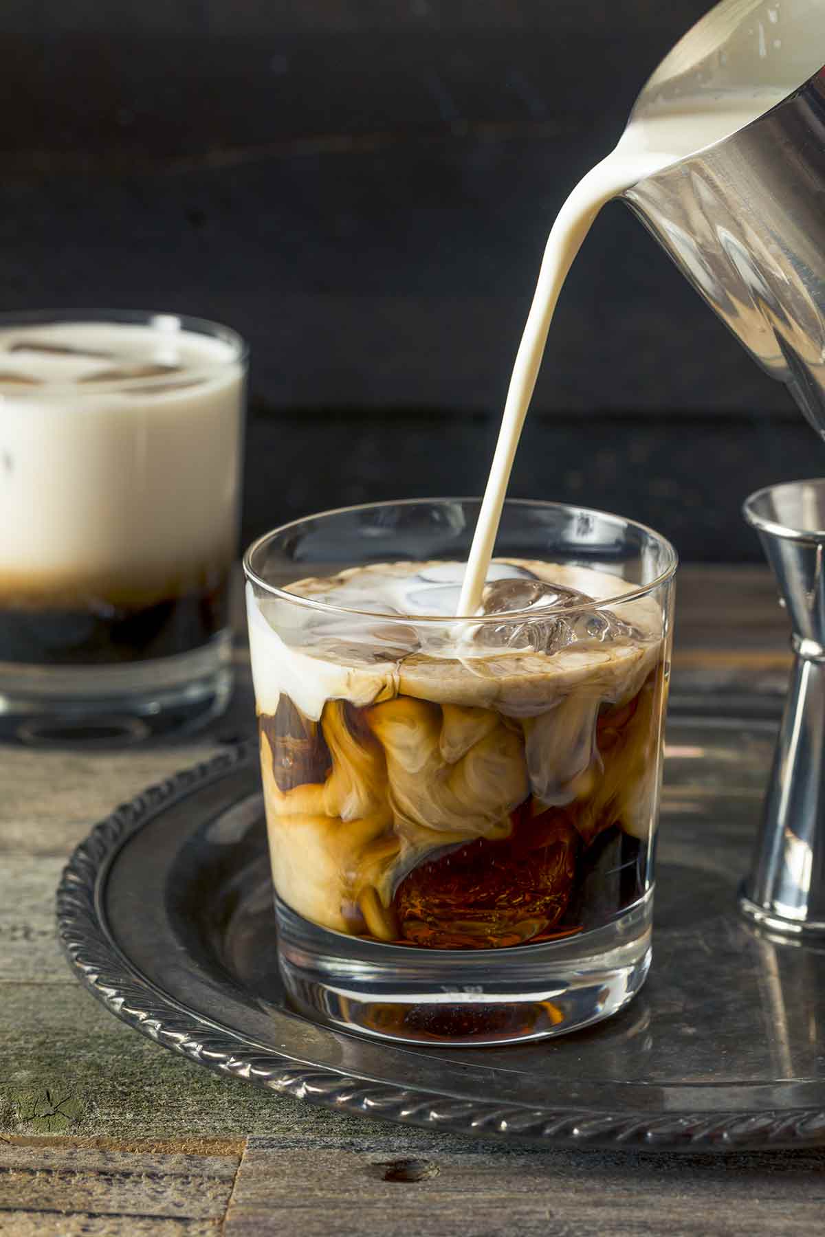 Cream being poured from a pitcher into a highball glass for a white Russian cocktail.