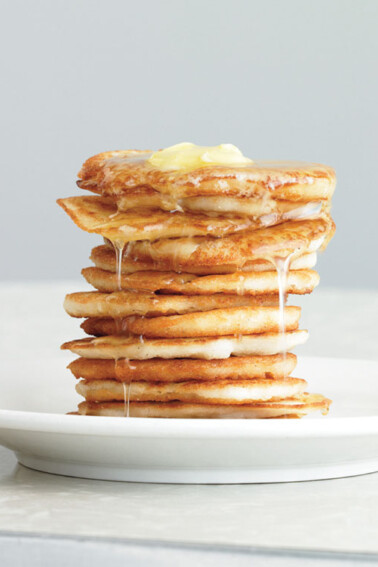 A stack of johnnycakes on a white plate topped syrup and butter.