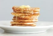 A stack of johnnycakes on a white plate topped syrup and butter.