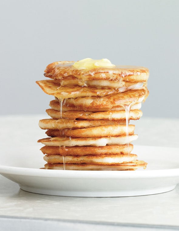 A stack of johnnycakes on a white plate topped syrup and butter.