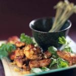 Port-paprika chicken bites garnished with cilantro, piled on a square white plate with a dish of picks.